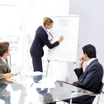 Businesswoman Writing on White Board and Businessman at Table